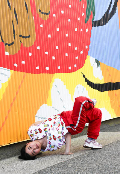 Inverted hiphop dancer outside, wearing graphic top and red pants